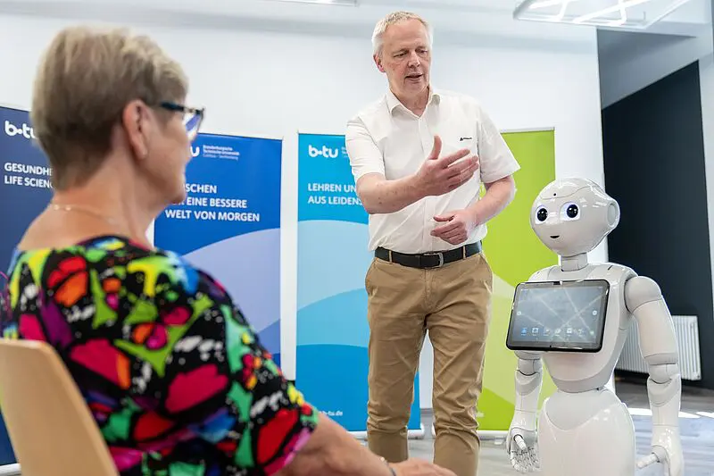 Interaktion Mensch - Roboter. Simulationspatientin (li.) im Dialog mit Pepper zum Trinkverhalten. Der BTU-Pflegewissenschaftler Jörg Matthäi gibt Erläuterungen. | Quelle: Foto: BTU, Sascha Thor 